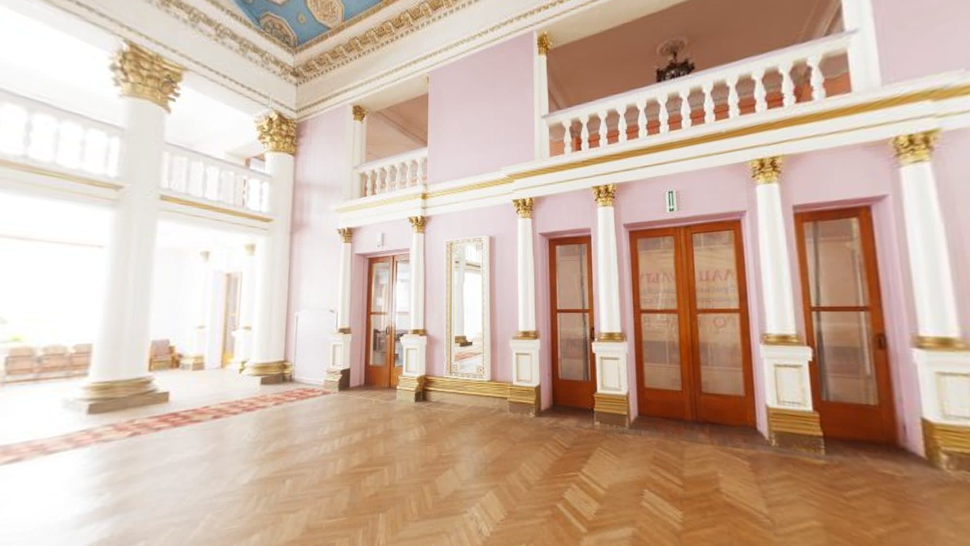 Grand banquet hall with white columns, gilded capitals, a balcony and herringbone parquet floor